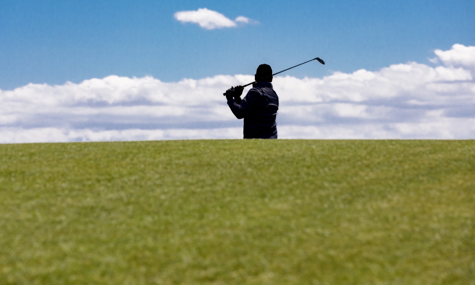 A golfer silhouetted against the sky, club high in the follow-through, on the crest of a fairway